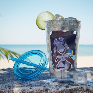 以下が含まれることがあります： ストローと蓋が付いた透明なプラスチック製のタンブラー。タンブラーには、帽子をかぶってビーチボールを持っている女性のデザインが施されています。タンブラーは氷とライムのくさびで満たされています。