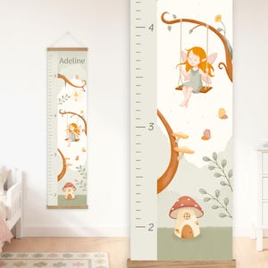 May include: A vertical wall-hanging growth chart featuring a light-colored background with a printed illustration of a fairy on a swing, a mushroom house, and foliage. The name Adeline is printed at the top, and the chart includes imperial markings.