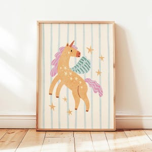 May include: A framed print featuring a whimsical unicorn illustration. The unicorn is depicted in shades of orange and pink, adorned with star accents. The background has vertical blue stripes on a cream-colored backdrop, with scattered gold stars.