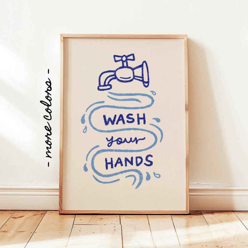 May include: A framed art print with a light beige background. The artwork features a blue illustration of a faucet with water droplets and the text "WASH your HANDS" in a whimsical font. The frame is a light wood color.