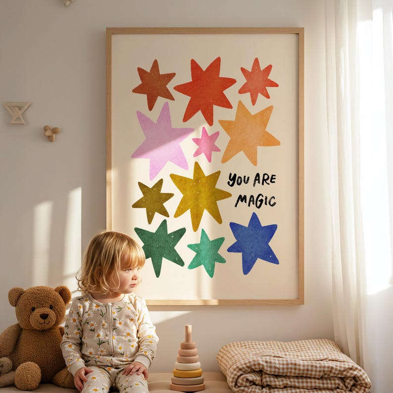 May include: A framed art print featuring colorful star illustrations in shades of orange, pink, yellow, green, and blue. The text "YOU ARE MAGIC" is written in black. The artwork is displayed in a child's room with a teddy bear and a child.