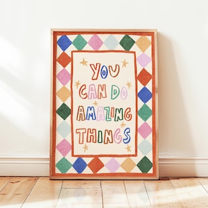 Può includere: Una stampa artistica incorniciata con le parole "You Can Do Amazing Things" in lettere colorate. L'opera presenta uno sfondo color crema con un bordo rosso e un motivo di diamanti colorati.