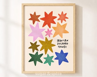 Puede incluir: Una lámina artística enmarcada con una colección de estrellas multicolores en tonos rojo, naranja, amarillo, rosa, verde y azul sobre un fondo crema. El texto "YOU CAN DO HARD THINGS" está impreso en negro en la parte inferior derecha.