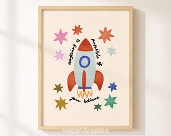 Op de afbeelding: Een ingelijste kunstdruk met een centrale illustratie van een raket in lichtblauw, rood en oranje. De tekst "Anything is possible if you believe" staat in zwarte schrijfletters rond de raket, omringd door kleurrijke sterren in diverse tinten.