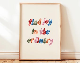 May include: A framed print with the words "find joy in the ordinary" in colorful, whimsical lettering. The text is in red, blue, green, orange, and pink. The print is displayed on a cream-colored background, framed in a light wood.