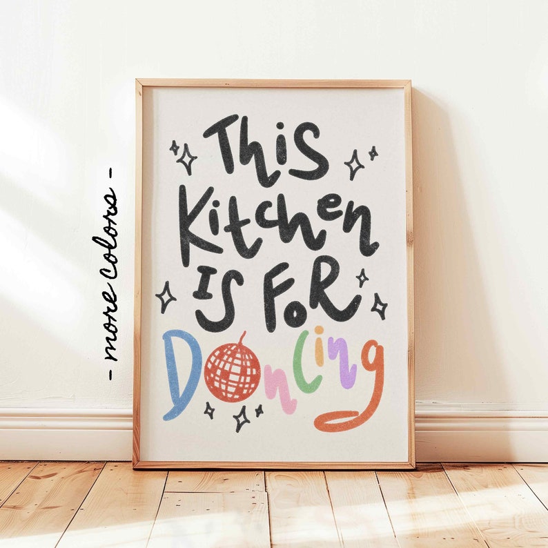 May include: A framed art print with the words "This Kitchen Is For Dancing" in black, blue, red, green, and orange. The print features a disco ball illustration and star accents. The frame is a light wood color.