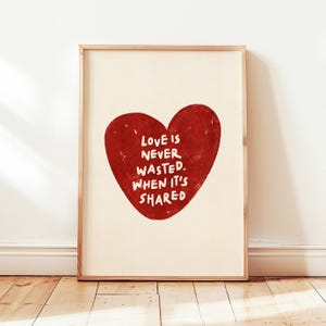 Puede incluir: Impresión enmarcada con un gran corazón rojo y la frase blanca "LOVE IS NEVER WASTED. WHEN IT'S SHARED". La obra se presenta sobre un fondo crema, enmarcada en madera natural, ideal para decoración.