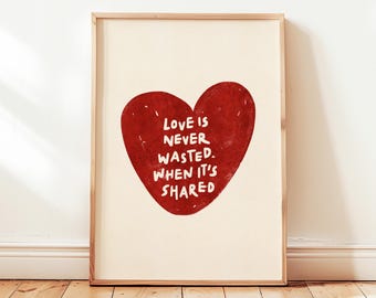 May include: A framed print featuring a large red heart with the words "LOVE IS NEVER WASTED. WHEN IT'S SHARED" in white lettering. The artwork is displayed on a cream-colored background, framed in natural wood.