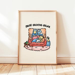 May include: A framed art print featuring a cartoon illustration of a cat relaxing on a red couch. The cat is under a blanket, with a window behind it showing a moon and clouds. The text "PAUSE. BREATHE. RELAX" is at the top.