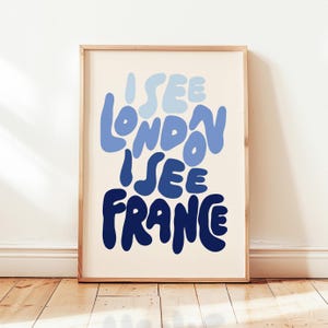 May include: A framed art print with the text "I SEE LONDON I SEE FRANCE" in shades of blue. The words are in a playful, rounded font against a cream-colored background. The frame is a light wood color.