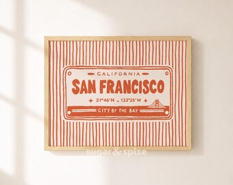May include: A rectangular framed print featuring a light-colored background with vertical orange stripes. The center displays a graphic resembling a license plate with the text CALIFORNIA, SAN FRANCISCO, 37°46'N 122°25'W, and CITY BY THE BAY.
