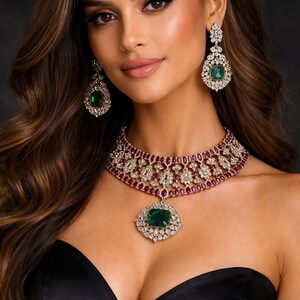 May include: A jewellery set consisting of a choker necklace and matching drop earrings. The necklace features a central emerald-cut green stone, surrounded by clear crystals and accented with small red stones. The earrings mirror this design.
