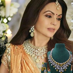 May include: A woman wearing a gold and white saree with a diamond necklace and earrings. The necklace and earrings feature yellow and white stones. The necklace is displayed on a green velvet stand.