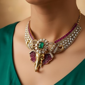 May include: A gold-toned statement necklace featuring an elephant pendant with a green emerald center stone. The necklace has ruby and diamond accents, and is worn against a green top.