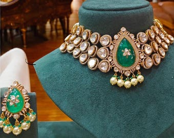 May include: A gold necklace with a large emerald green gemstone pendant surrounded by smaller diamonds. The necklace is on a green velvet display stand. A pair of matching earrings with emerald green gemstones and pearl accents are also shown.