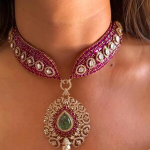 Peut inclure: Un collier en or avec un grand pendentif orné d'une pierre précieuse verte entourée de petites pierres précieuses rouges et blanches. Le collier est en or et présente une chaîne délicate.