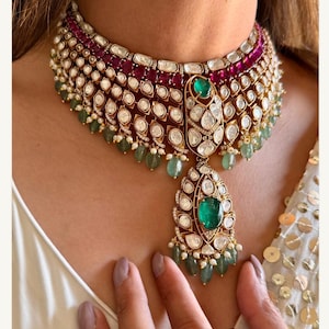 Puede incluir: Un collar gargantilla de oro con un colgante en forma de lágrima. El collar está adornado con diamantes redondos y rectangulares, rubíes rojos y esmeraldas verdes.