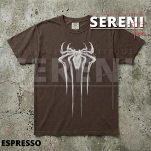 Puede incluir: Camiseta color espresso con un gr&aacute;fico de ara&ntilde;a blanco. El dise&ntilde;o incluye la palabra "SERENI" en rojo y blanco, y la palabra "ESPRESSO" en la parte inferior. La camiseta tiene cuello redondo y mangas cortas.