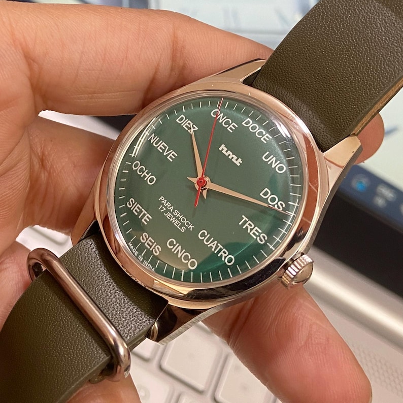 Puede incluir: Un reloj de pulsera con esfera verde y caja dorada. La esfera muestra la hora con agujas doradas y n&uacute;meros espa&ntilde;oles. El reloj tiene una correa de cuero verde y el texto "PARA SHOCK 17 JEWELS".