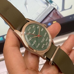 Puede incluir: Un reloj de pulsera con esfera verde y caja dorada. La esfera muestra n&uacute;meros en espa&ntilde;ol y el texto "PARA SHOCK 17 JEWELS". La correa es de cuero verde.