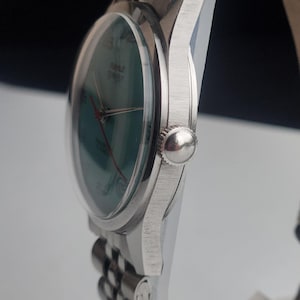 May include: A silver wristwatch with a green face and red hands. The watch has a clear, domed crystal and a silver band. The watch face has the word "TIME" printed on it. The watch is a classic style.