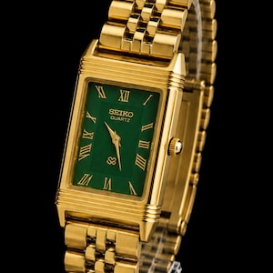 May include: A gold-tone rectangular wristwatch featuring a vibrant green dial with gold Roman numeral hour markers. The watch includes a matching gold-tone metal link bracelet, gold hands, and the text Seiko Quartz printed on the watch face.