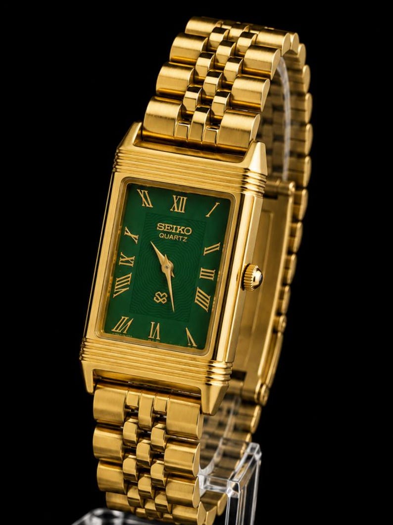 May include: A gold-tone rectangular wristwatch featuring a vibrant green dial with gold Roman numeral hour markers. The watch includes a matching gold-tone metal link bracelet, gold hands, and the text Seiko Quartz printed on the watch face.