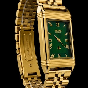 May include: A gold-tone rectangular wristwatch featuring a vibrant green dial with gold Roman numeral hour markers. The watch includes a matching gold-tone metal link bracelet and displays the text SEIKO QUARTZ on the face. The clasp is engraved with STAINLESS STEEL.