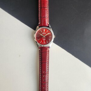 May include: A red wristwatch with a silver bezel and a matching red leather band. The watch face is red with silver hands and markers. The band has a crocodile texture and white stitching.