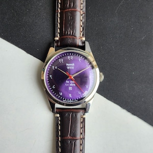 Könnte beinhalten: Eine Armbanduhr mit lila Zifferblatt und braunem Lederarmband. Das Zifferblatt hat arabische Ziffern und rote Zeiger. Das Uhrengehäuse ist silberfarben. Das Armband ist dunkelbraun mit Krokodilmuster.