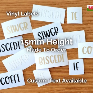 May include: A collection of white vinyl labels with custom text in black and beige fonts. The labels are 15mm high and made to order. The image also includes the text "Vinyl Labels" and "Custom Text Available".