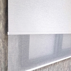 May include: White and gray double roller shades with a textured fabric. The shades are partially rolled up, revealing the white fabric underneath.