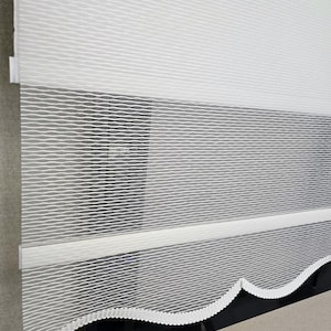 Puede incluir: Persiana blanca de varias capas con un borde inferior festoneado. La persiana presenta un patrón texturizado en forma de onda. La capa superior es opaca, mientras que la capa inferior es semitransparente.