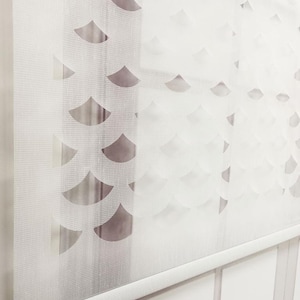 May include: White sheer window blind with a repeating pattern of cut-out scallops. The blind is rolled up and the white roller mechanism is visible.