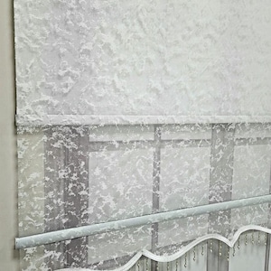 May include: White sheer window blind with a textured pattern and a scalloped bottom edge with silver beads.