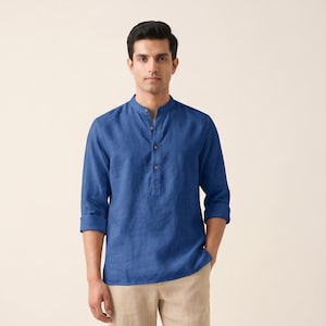 May include: A man wearing a blue Henley shirt with a mandarin collar and beige pants. The shirt has long sleeves and a button-down placket. The pants are a light tan color. The man is wearing brown sandals.
