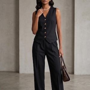 Könnte beinhalten: Ein schwarzes, ärmelloses Oberteil mit goldenen Knöpfen und eine passende Hose mit weitem Bein. Das Outfit wird mit einer braunen Handtasche und einer Perlenkette kombiniert. Ein klassischer, eleganter Stil.