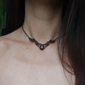 Op de afbeelding: Een bruine macramé choker ketting met een donkerpaarse edelsteen hanger.