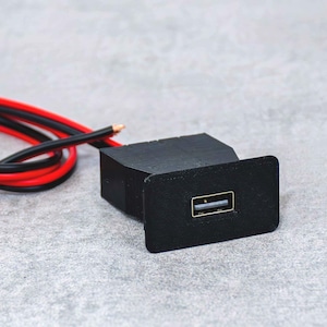 May include: A black USB port with a rectangular faceplate. The port has a standard USB connection. Red and black wires extend from the back of the port. The item is on a grey surface.