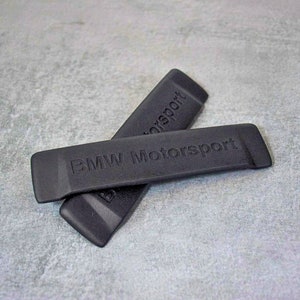 Könnte beinhalten: Zwei schwarze Ventilkappen mit dem geprägten Text "BMW Motorsport".