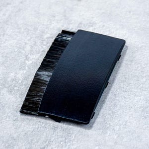 以下が含まれることがあります： 長方形の黒いカバーが付いた黒いブラシストリップ。ブラシの毛は黒色で、カバーの片側から伸びています。このアイテムはおそらく、シーリングまたはクリーニングに使用されます。