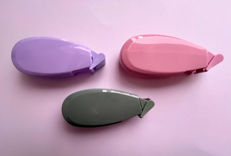 Peut inclure: Trois distributeurs de ruban adh&eacute;sif de couleurs diff&eacute;rentes&nbsp;: violet, rose et gris. Chaque distributeur est dot&eacute; d'une petite lame pointue pour couper le ruban.