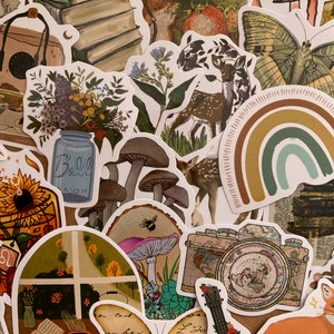 May include: A collection of colorful stickers featuring various nature-inspired designs, including mushrooms, butterflies, deer, a rainbow, a camera, a guitar, a sunflower, a mason jar, a book, and a cup of tea. The stickers are printed on white paper and have a glossy finish.