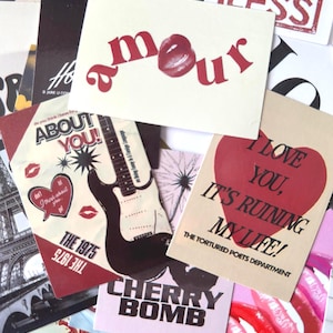May include: A collection of various cards with text and graphics. One card reads "amour" with a lip graphic. Other cards feature phrases like "About You!", "Cherry Bomb", and "I Love You, It's Ruining My Life!" in red and black.