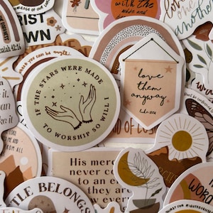 Pode incluir: Uma coleção de autocolantes inspiradores com vários designs e citações. Os autocolantes apresentam frases como "If the stars were made to worship so will I" e "love them anyway". As cores incluem bege, castanho e branco.