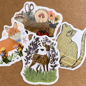 May include: Four illustrated stickers featuring a fox in a field of flowers, a deer in a forest, a cat with text from a book, and a basket with sewing supplies and a mushroom.