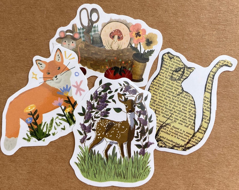 May include: Four illustrated stickers featuring a fox in a field of flowers, a deer in a forest, a cat with text from a book, and a basket with sewing supplies and a mushroom.