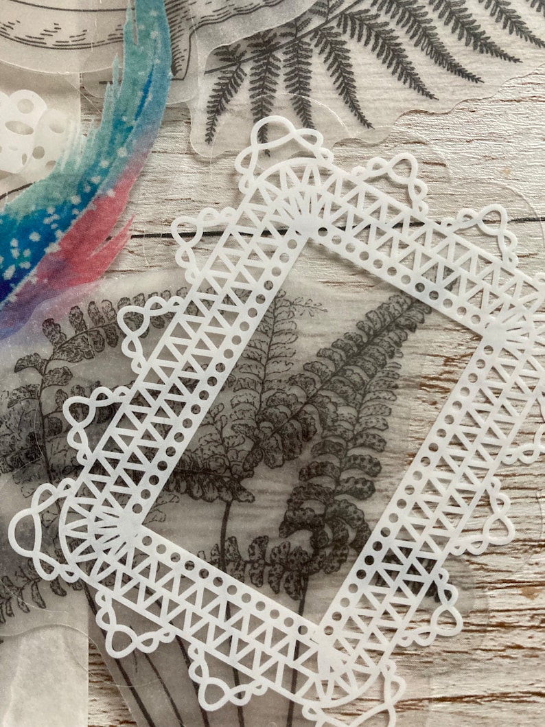 May include: White decorative frame with a delicate lace design. The frame is made of a thin, translucent material and has a square shape. The frame is perfect for adding a touch of elegance to any project.