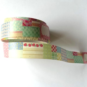 Könnte beinhalten: Eine Rolle dekoratives Washi-Tape mit einem Patchwork-Design. Das Klebeband weist verschiedene Muster auf, darunter Quadrate, Erdbeeren und florale Motive, in Pastellfarben wie Rosa, Grün und Gelb. Das Klebeband hat leere Etikettenformen.