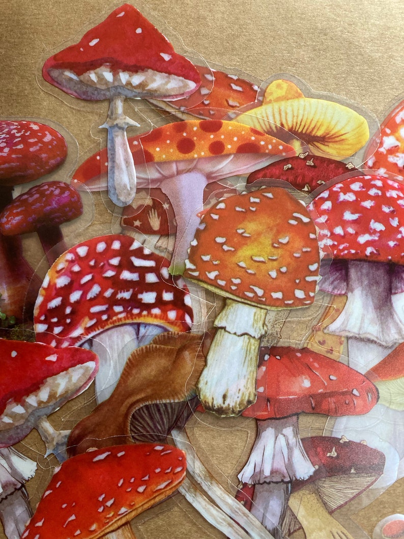 May include: A collection of red and white mushroom stickers with brown stems. The mushrooms are arranged in a random pattern and are all different sizes. The stickers are on a brown background.